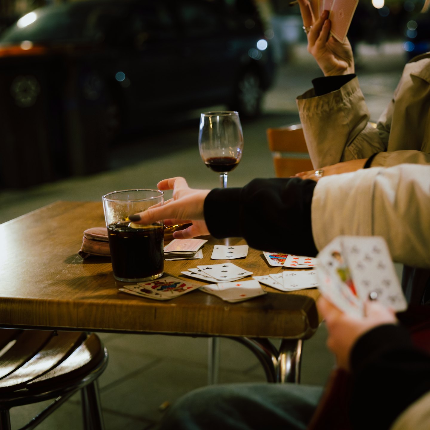 Hands play cards around a table with drinks.