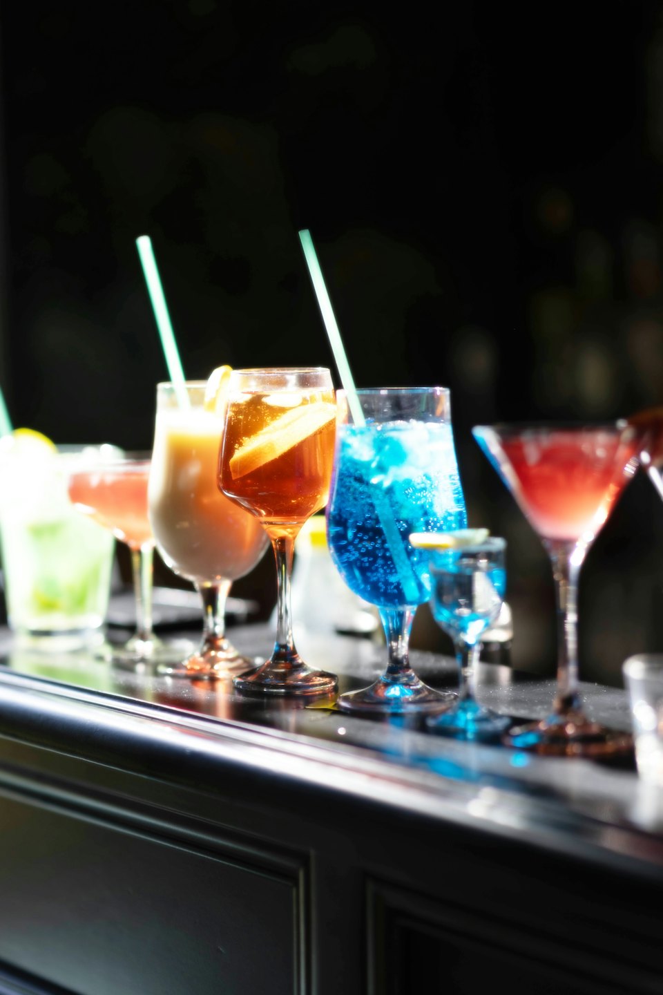 Colorful cocktails arranged on a dark bar counter.