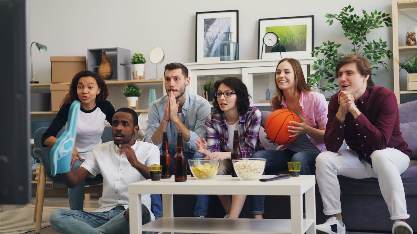Five friends watch a sports game together in a living room.
