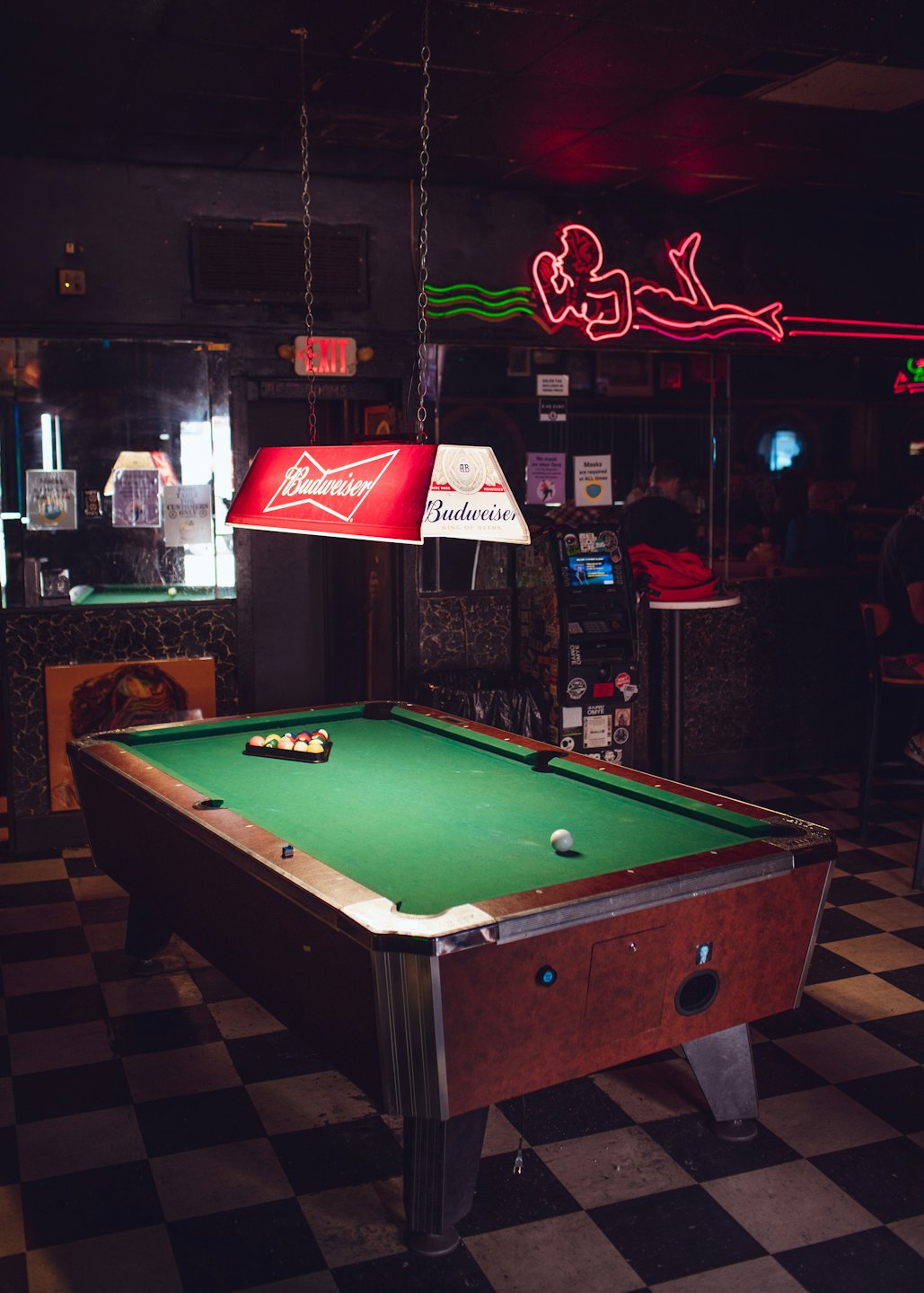 Pool table with racked balls stands in a dimly lit bar.