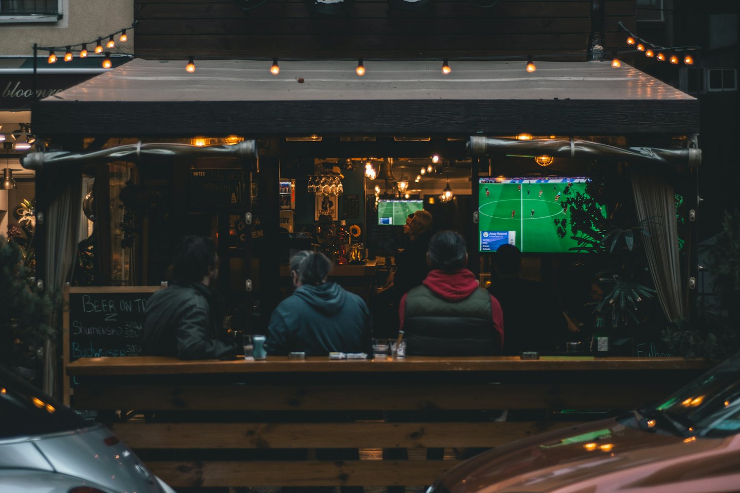 Men watch football on TV at an outdoor bar counter.
