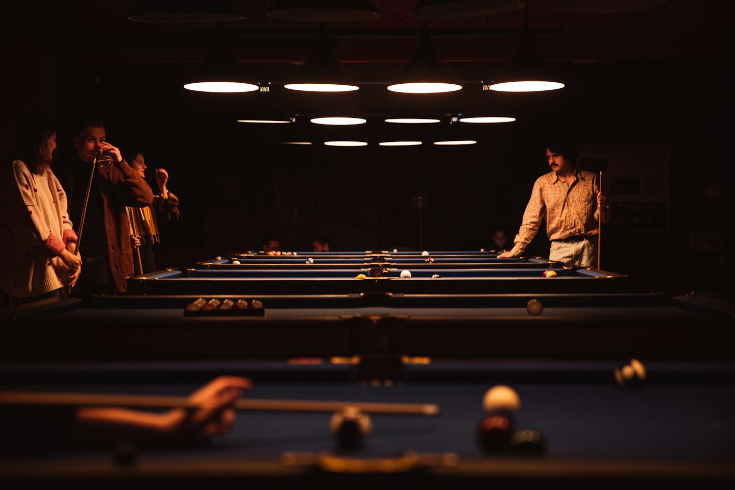 Man plays billiards in a dimly lit hall with blue tables.