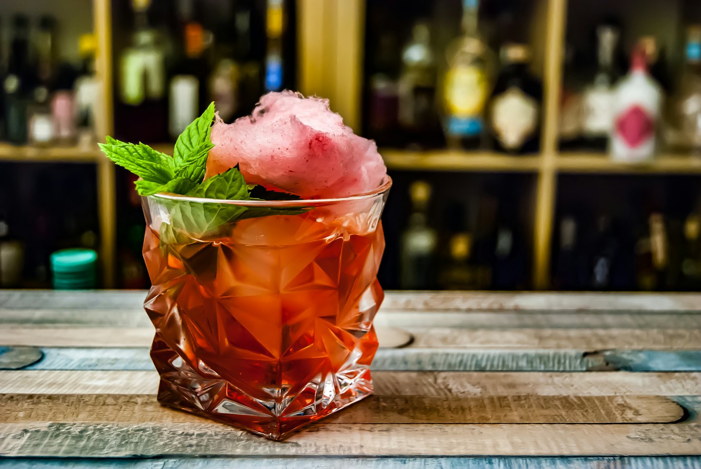 A sweet cocktail with cotton candy and mint on a wooden bar.