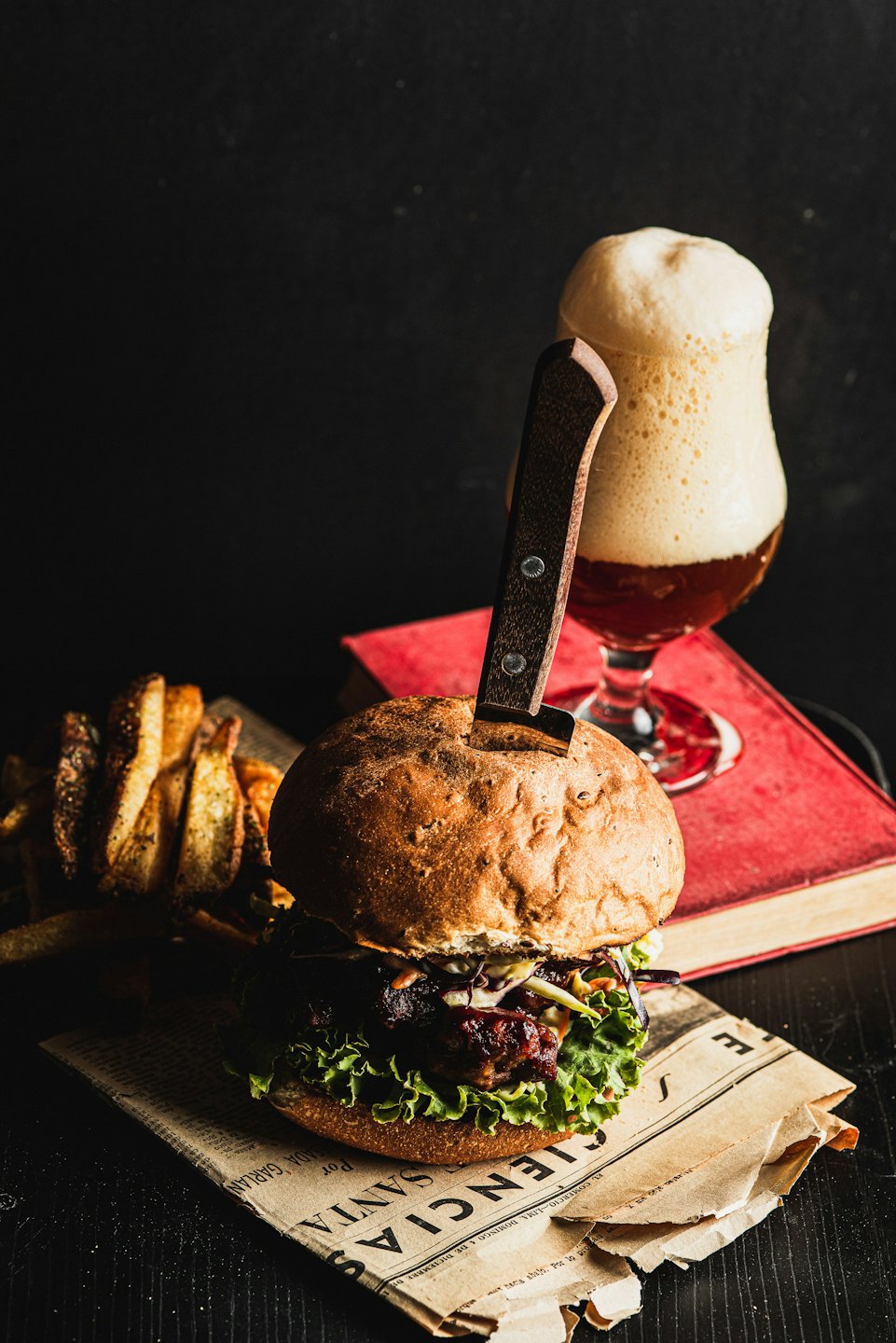 A gourmet burger with a knife sits beside fries and beer.