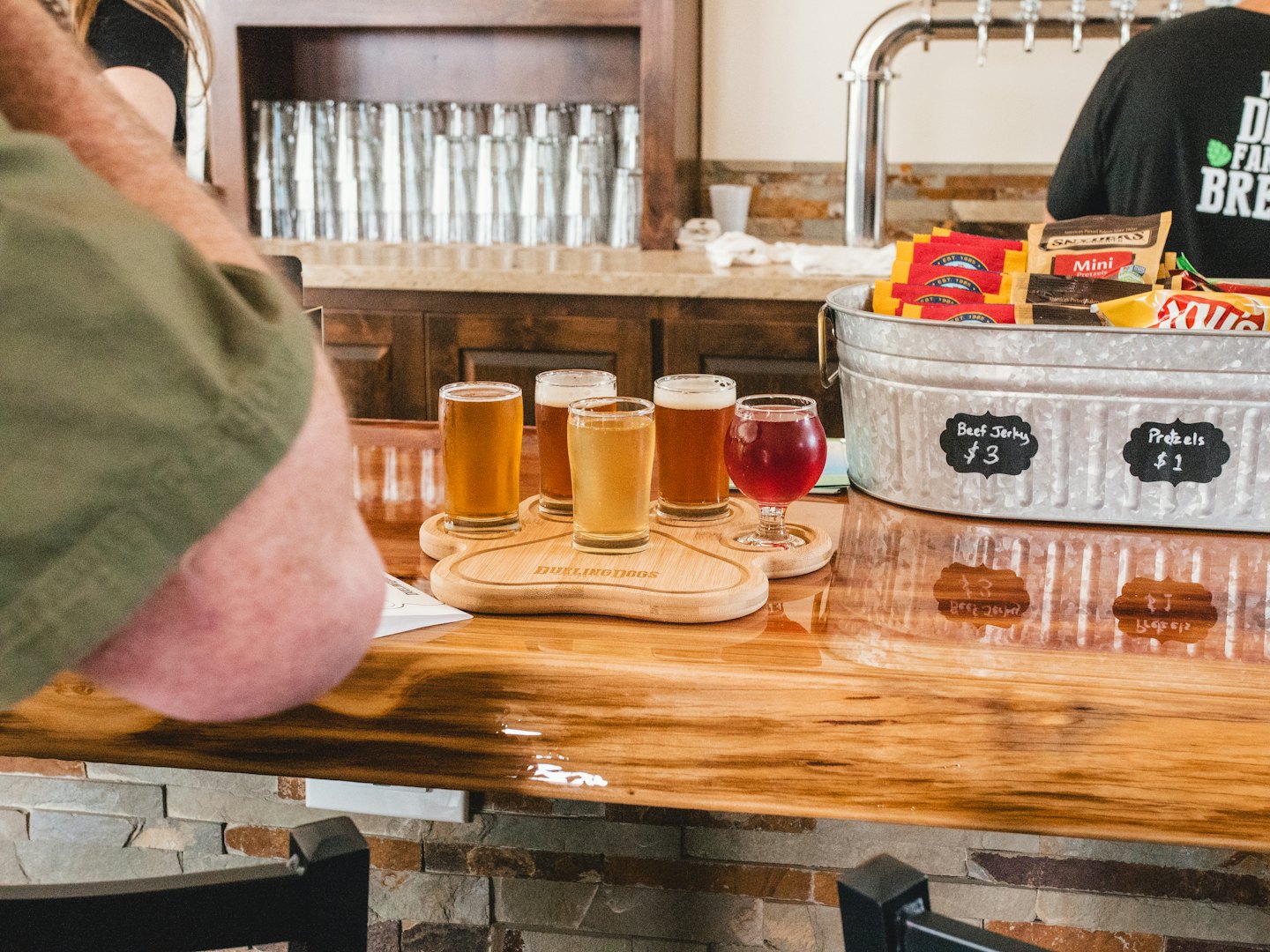 Four beers and one red drink on a branded paddle on a wooden bar.