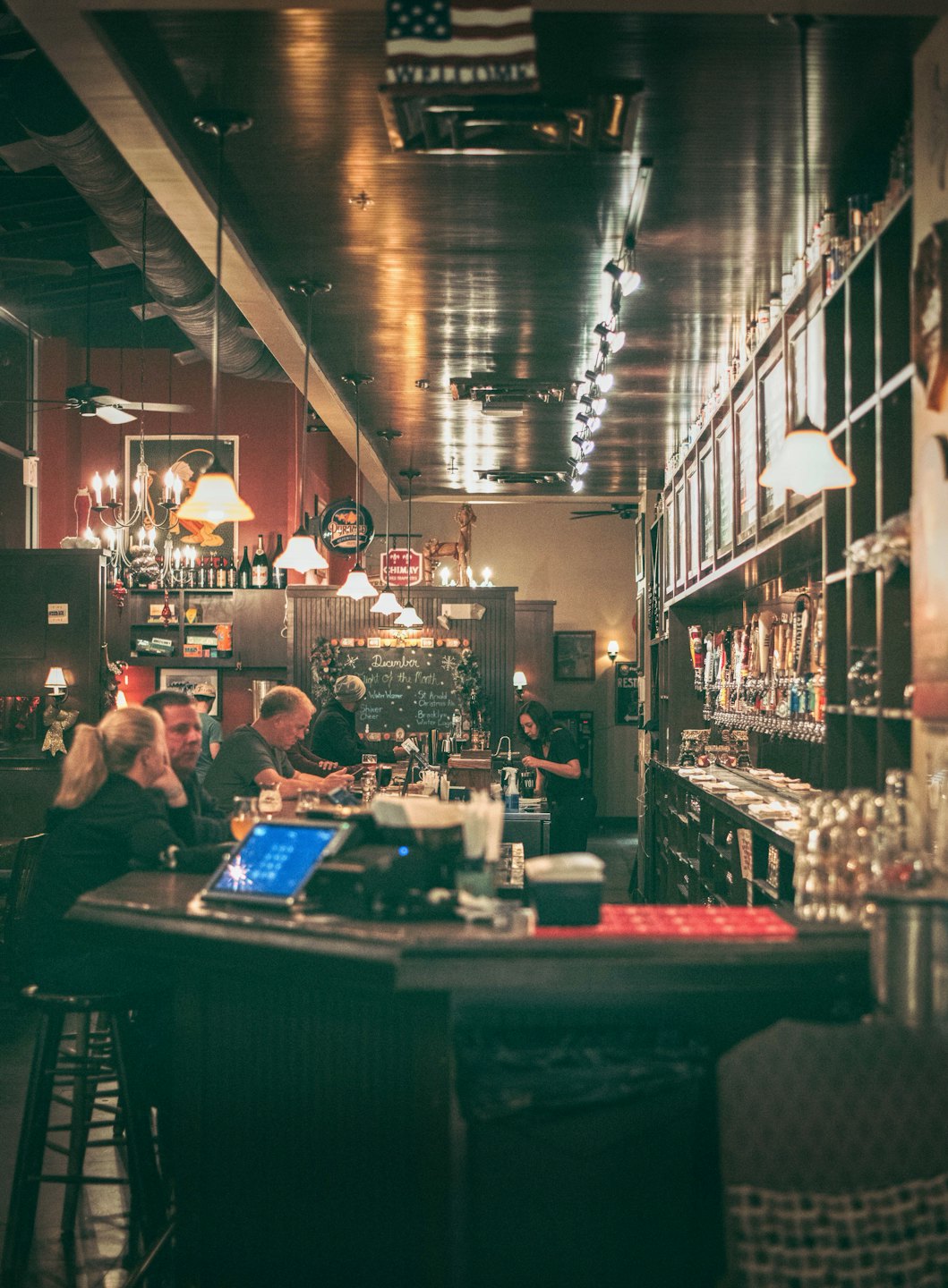 Patrons socialize at a pub counter while the bartender serves drinks.